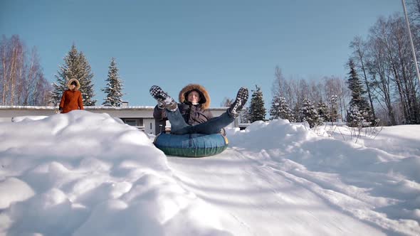 Funny Man is Rolling Down a Hill on an Inflatable Snowtube Showing Peace Gesture