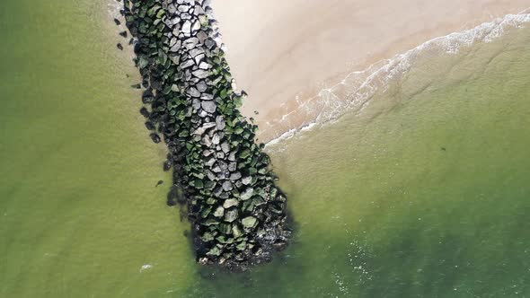 a top down shot of a stone jetty. The drone camera ascends, while rotating clockwise to reveal more