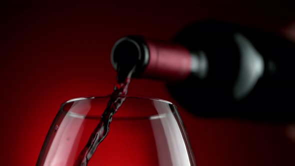 Super Slow Motion Detail Shot of Pouring Red Wine From Bottle on Luxury Red Background at 1000Fps