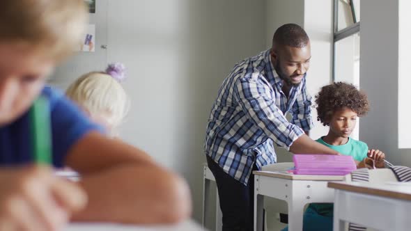 Video of happy african american male teacher helping biracial boy during lessons