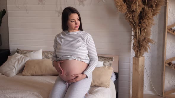 Pregnant Woman in the Bedroom on the Bed She Stroking Her Tummy with Her Hands