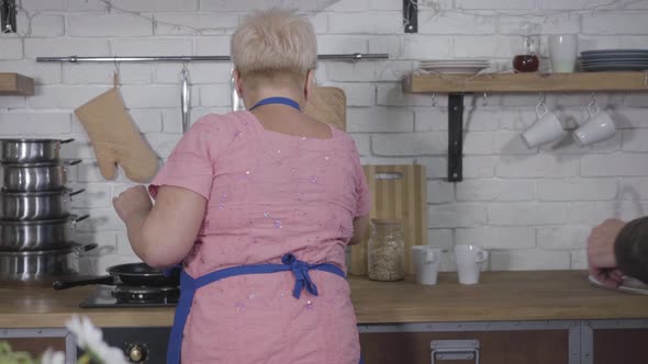 Back View of Senior Blond Caucasian Woman Getting Bouquet of Yellow Tulips While Cooking at the