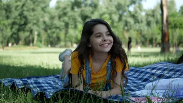 A small and very beautiful girl lying on the grass, smiling sincerely