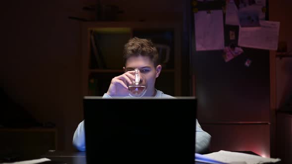 A young guy is studying at the computer at night