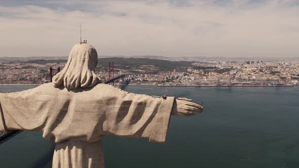 Open arms Cristo Rey overlooking Lisbon cityscape and 25 de Abril Bridge over tagus river.