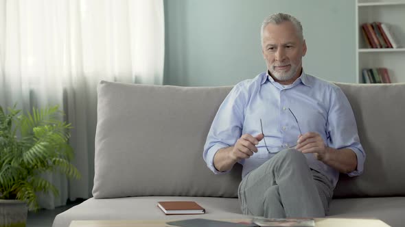 Healthy Senior Man Sitting on Sofa, Wearing Eyeglasses, Dreaming About Holiday