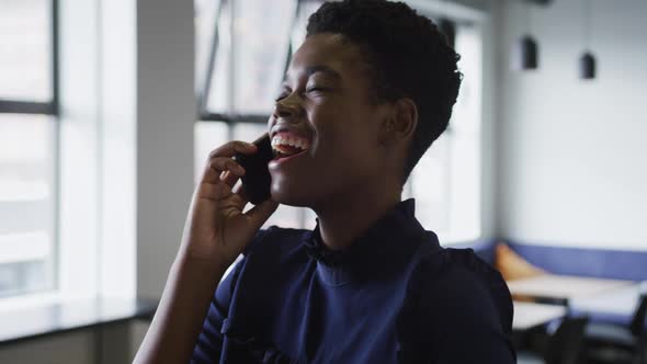 Smiling mixed race businesswoman standing talking on smartphone in office