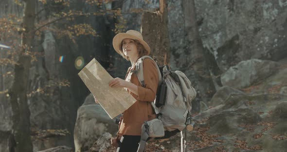 Attractive young woman in stylish hat and a tourist map in her hands looking around