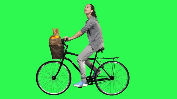 Casual woman riding a bicycle over a green screen, looking around and smiling. 4K