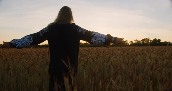 Young womaan in national Ukrainian clothes walking on a field of wheat at sunset