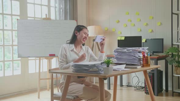 Asian Woman Being Upset Losing Game On Smartphone After Working With Documents At The Office