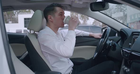 Portrait of Young Man Businessman in White Shirt Sitting in the Car and Drinking Coffee