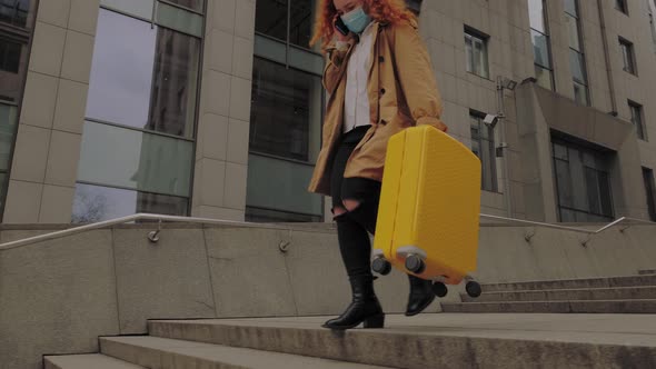 European Woman Going with Yellow Suitcase and Talks on the Phone in Protective Face Mask