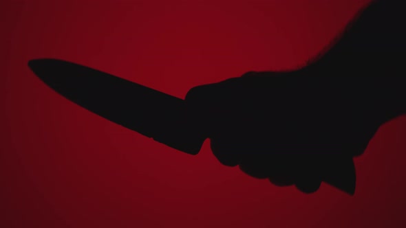 Close-up silhouette of a man's hand with a large knife against a red background