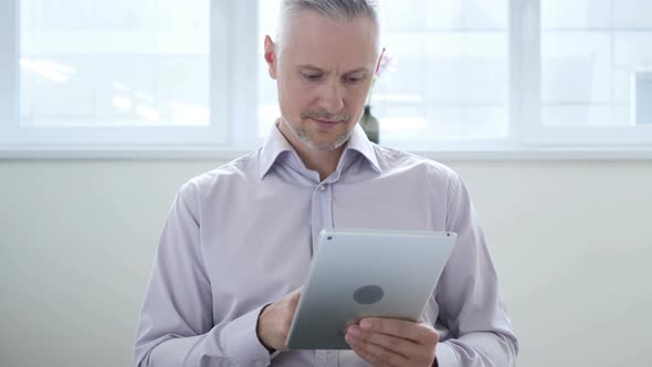 Middle Aged Man Browsing Internet on Tablet in Office