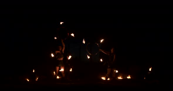 Three Women with Burning Hoops Dance with Fiery Torches in Leather Clothes in a Dark Hangar