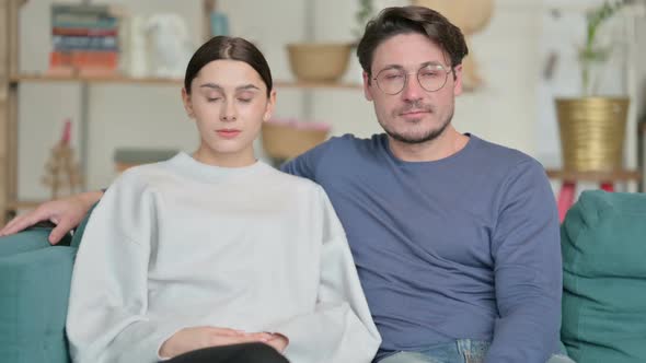 Couple Looking at Camera While Sitting on Sofa