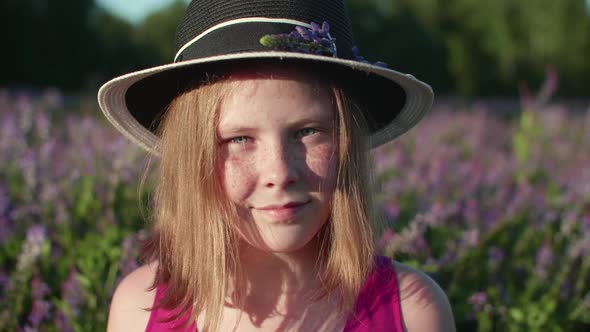 Portrait Freckled Girl in Hat on Flowering Violet Field in Summer Countryside