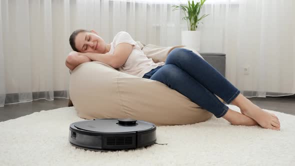 Young Woman Sleeping in Living Room Next to Working Robot Vacuum Cleaner