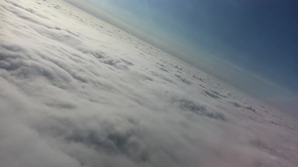 Above the clouds - filmed at a dutch angle from a passenger airliner. Daytime, blue sky, atmospheric