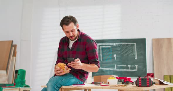 A Carpenter Uses a Smartphone During a Break at Work Young Handsome Craftsman is Resting in a