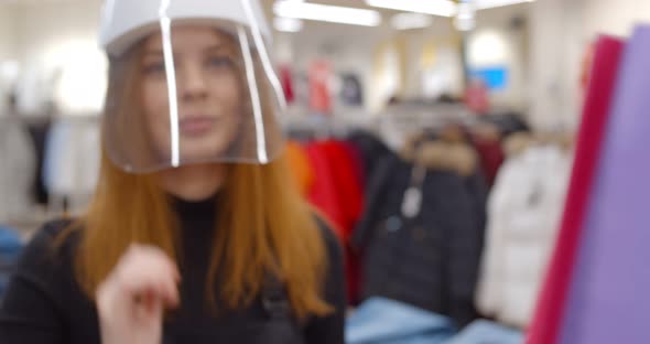 Clothes Store Seller in Plastic Face Shield Giving Bag with Purchase To Client