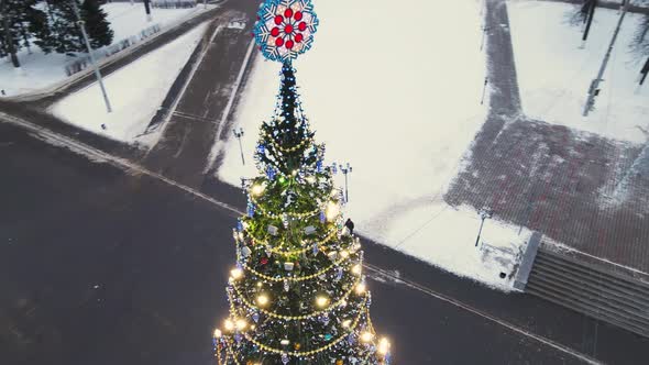 A Slender Luminous Christmas Tree on the City Square Aerial View