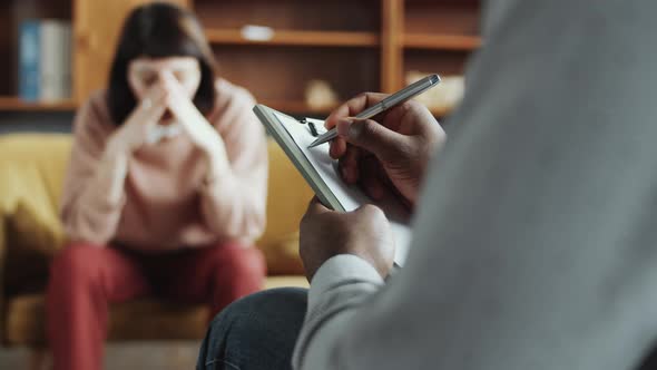 Hands of Male Black Counselor Taking Notes during Consultation with Woman