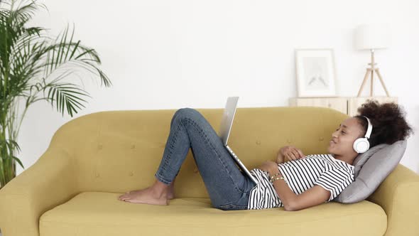 African Woman Having a Video Call on Laptop Computer While Lying on Sofa at Home