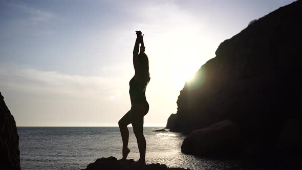 Young Woman with Long Hair Practicing Stretching Outdoors on Yoga Mat By the Sea on a Warm Sunset