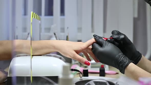 salon master in protective gloves manicures a client through a protective screen