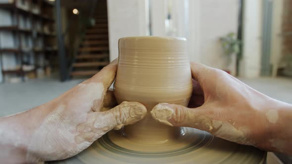 Close-up of Dirty Hands Shaping Clay Into Bowl on Potter's Wheel Working Indoors