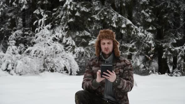 Hiker Man with Tablet in Hands in Winter in Snowy Forest