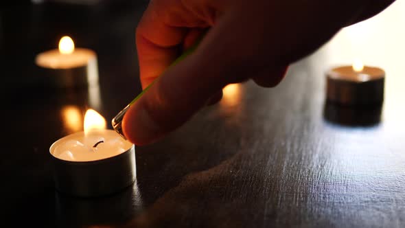 Lighting a single small tealight candle flame in slow motion with other fires burning and dancing in