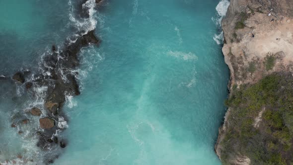 Top down aerial view of waves breaking inside a small, rocky bay