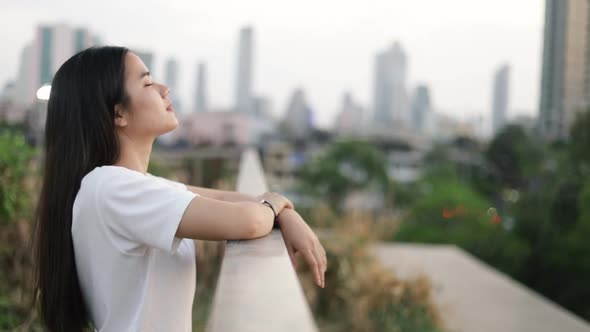 Portrait of beautiful Asian woman enjoying peaceful sunset and looking up exhaling fresh air.