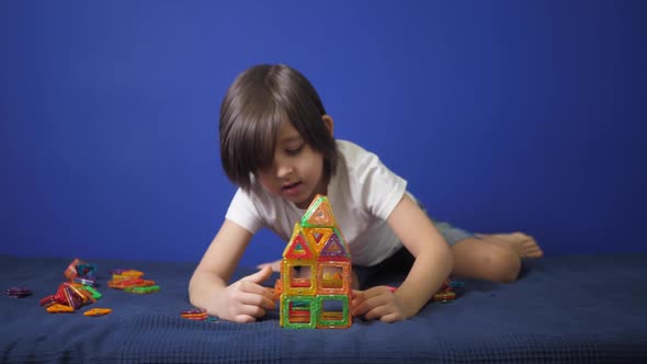 Boy Child in a White Tshirt is Sitting on a Bed Against a Blue Wall and Playing