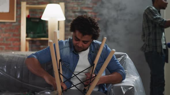 Black Man Assembles Chair and Colleague Paints Wall in Room