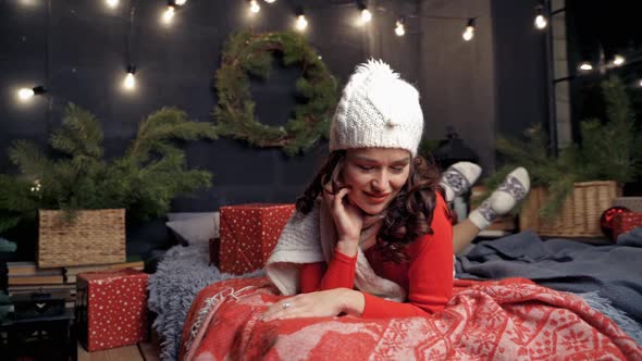 Woman in red sweater Santa and white hat laying on bed posing to the camera.