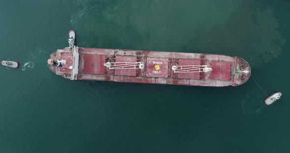 Large cargo ship enters the port escorted by tugboats.