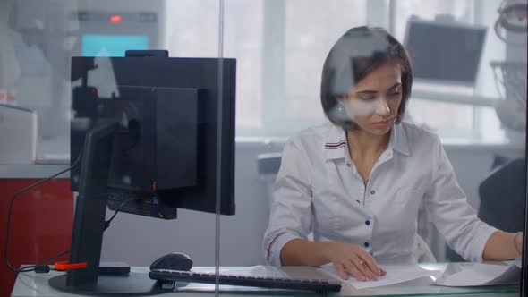 A Female Doctor Sits at a Table and Writes with a Pen Writing Out a Prescription To a Patient