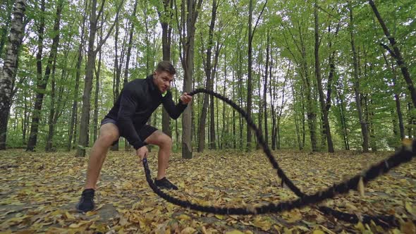 Male training with battle rope. Muscular man working out with battle ropes in park