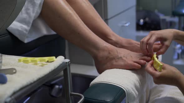 Pedicurist prepares feet with toe separator for painting.