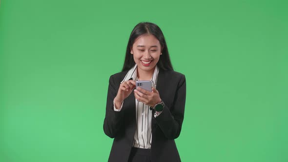 A Smiling Asian Business Woman Using Mobile Phone While Walking On Green Screen