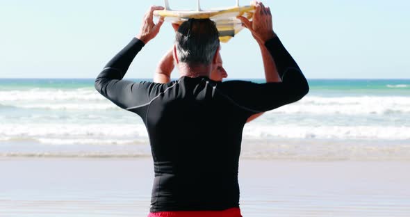 Senior couple carrying surfboard over head while walking towards the sea