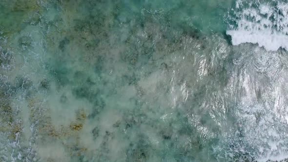 Aerial top-down view of waves crashing over a rocky bottom of a crystal clear Caribbean sea next to