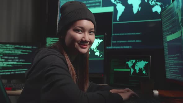 Young Asian Woman Hacker Using Computer Hacking, Looking And Warmly Smiles To Camera