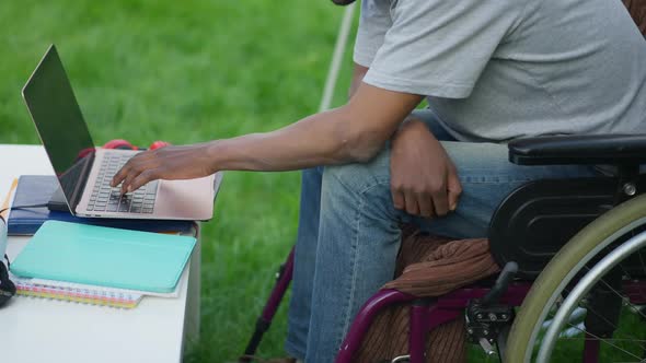 Unrecognizable African American Adult Man in Wheelchair Typing on Laptop Keyboard in Slow Motion