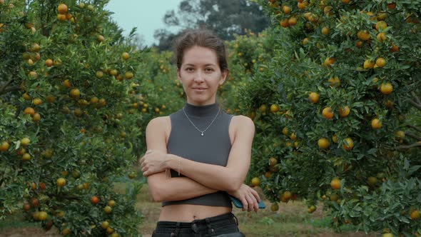 Girl Standing and Smiling in an Orange Orchard Looking Straight at the Camera