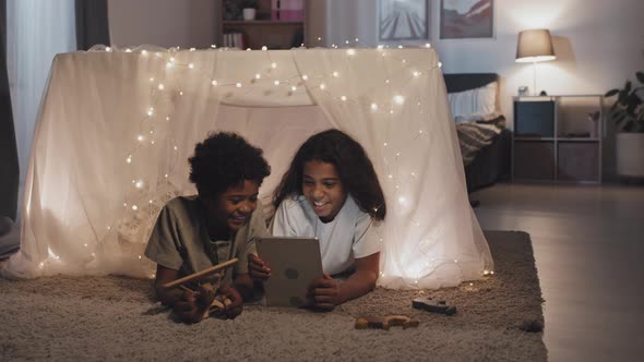 Siblings Using Tablet in Pillow Fort